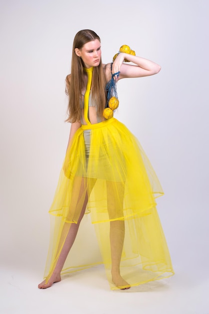 Una chica con un vestido amarillo con una bolsa de limones en un fondo blanco.