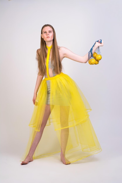 Una chica con un vestido amarillo con una bolsa de limones en un fondo blanco.