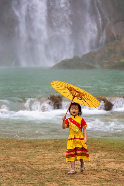 Una chica con un vestido amarillo y un paraguas vietnamita cerca de la cascada de Ban Jok. Vietnam