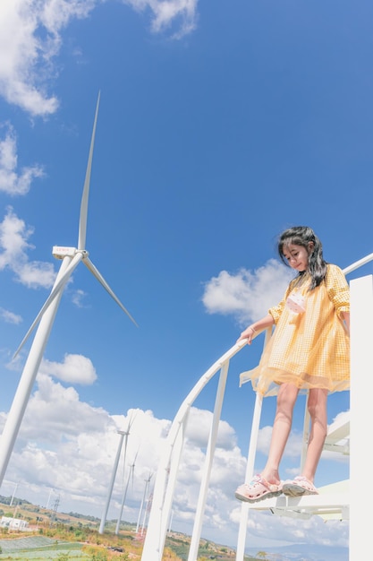 Una chica con un vestido amarillo se para en una plataforma blanca con un cielo azul de fondo.