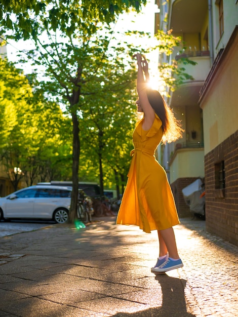 Una chica con un vestido amarillo de verano camina por la calle bajo los rayos del sol.