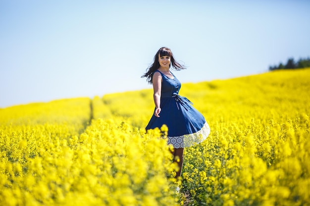 Chica con un vestido azul se va en un campo de colza Sígueme concepto