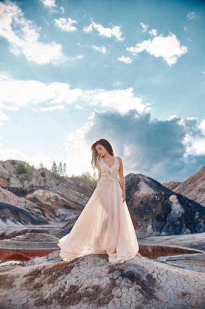 Chica en un vestido azul claro de pie en el viento con montañas