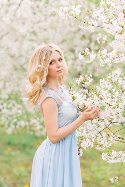 Chica con un vestido azul en el jardín de primavera. Sobre un fondo de flores blancas