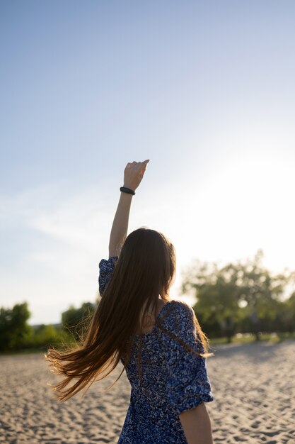 Chica con un vestido azul posando en la arena cerca del río. Mujer disfrutando de un clima soleado.