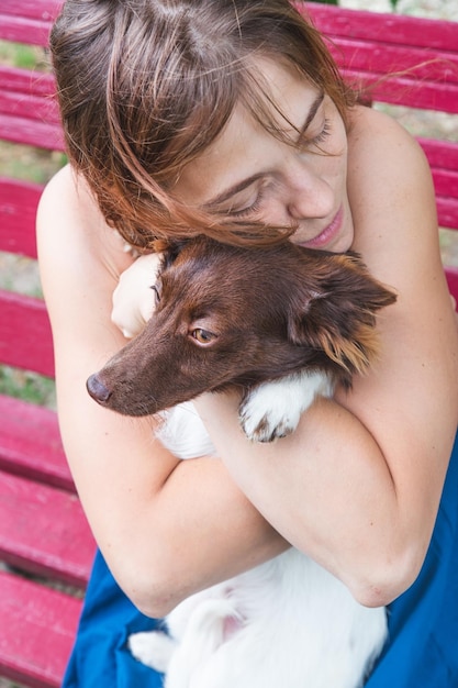 Foto una chica con un vestido azul se sienta en un banco y abraza a un pequeño perro marrón y blanco amor mascotas día del perro