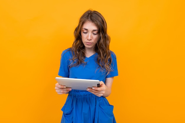 Chica en un vestido azul con una tableta en sus manos sobre un fondo amarillo y naranja con espacio de copia