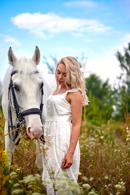 Chica en vestido blanco con un caballo en el campo