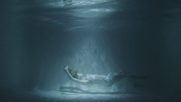 Una chica con un vestido blanco cae bajo el agua.