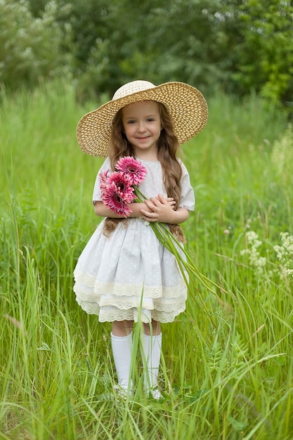 Chica con un vestido blanco en un campo de manzanilla. Niña abraza un ramo de margaritas y sonríe.