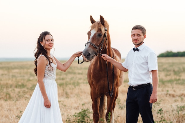 Una chica con un vestido blanco y un chico con una camisa blanca en un paseo con caballos marrones en el pueblo