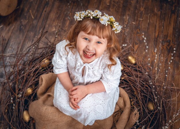 Chica con un vestido blanco con una corona de flores en la cabeza sentada en el nido