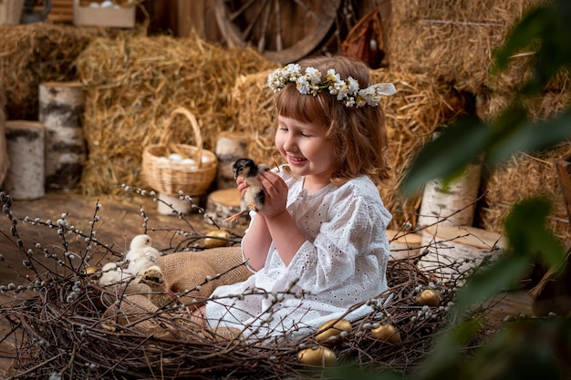 Chica con un vestido blanco con una corona de flores jugando con un pollo