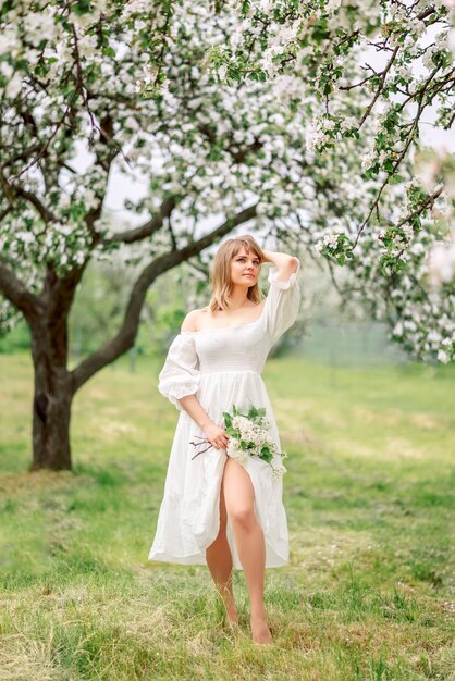 Foto una chica con un vestido blanco en un jardín de primavera con un ramo de flores.