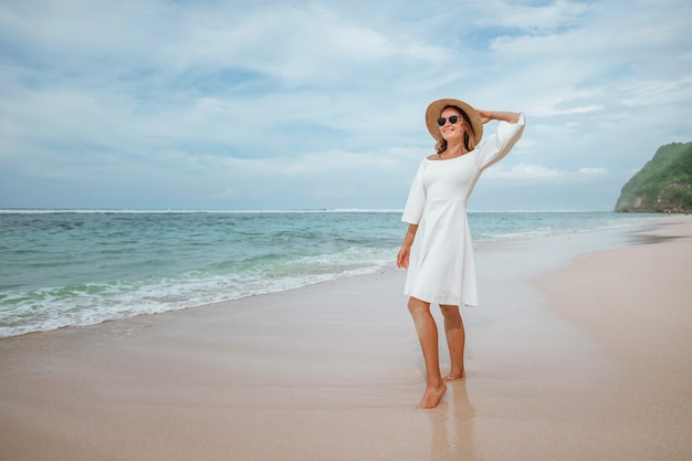 Chica con un vestido blanco en la playa con un sombrero y gafas de sol