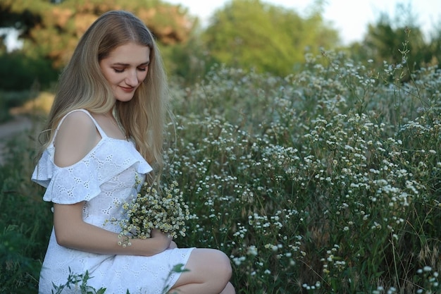 una chica con un vestido blanco se sentó y recogió flores silvestres