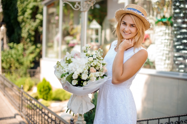 Chica con un vestido blanco y un sombrero de paja sostiene un ramo festivo