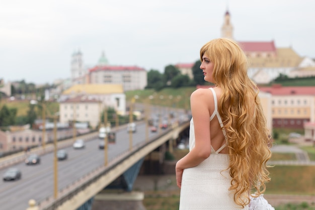 Una chica con un vestido blanco con sombrilla blanca posando sobre fondo de ciudad.