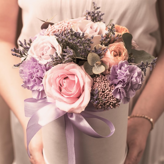 Una chica con un vestido blanco sostiene una caja redonda con flores: felicitaciones, vacaciones. Procesamiento de fotos antiguas y retro.