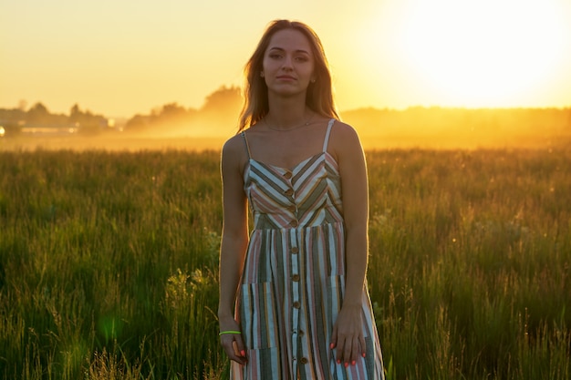 Una chica con un vestido en un campo verde bajo los brillantes rayos del sol poniente.