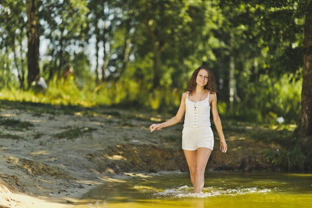 Chica en un vestido corto blanco camina a lo largo de la orilla del estanque 6332