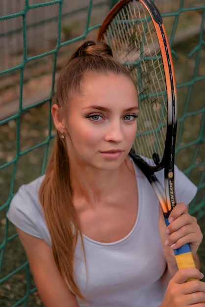 Una chica con un vestido deportivo blanco se para en una cancha de tenis y sostiene un retrato de raqueta de una chica en la cancha de tenis