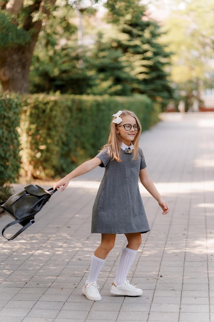 una chica con un vestido gris similar a uno de la escuela con gafas está girando con un maletín