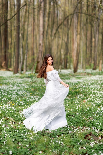 Una chica con un vestido largo blanco da vueltas en un claro con flores Una mujer joven con el pelo largo en un bosque primaveral