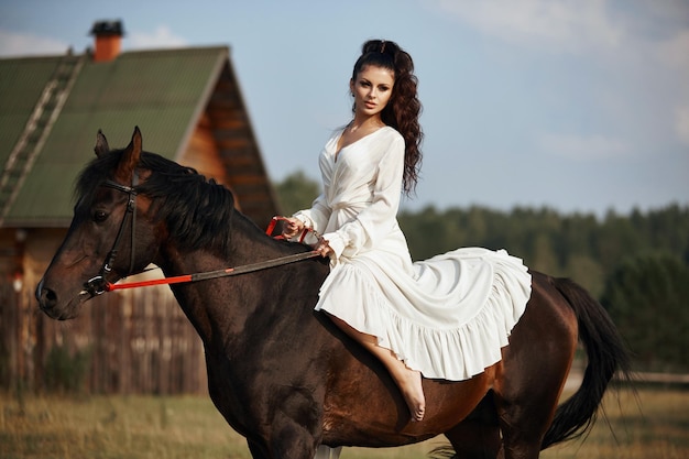 Chica con un vestido largo a caballo, una hermosa mujer a caballo en un campo en otoño. Vida y moda en el campo, noble corcel