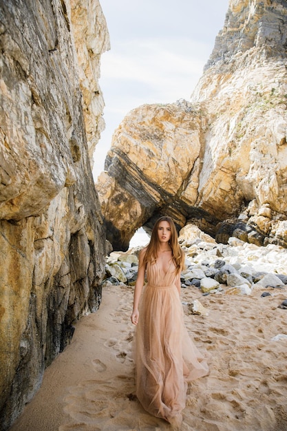 Chica en vestido largo cerca de rocas y océano.