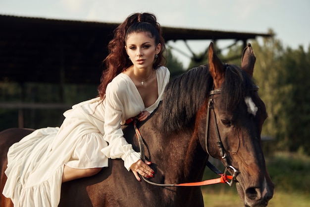 Chica en un vestido largo montando a caballo, una hermosa mujer montando un caballo en un campo en otoño.