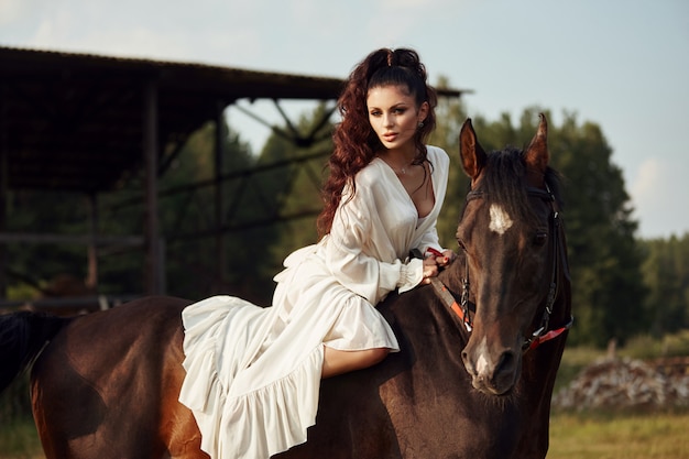 Chica en un vestido largo montando a caballo, una hermosa mujer montando un caballo en un campo en otoño.