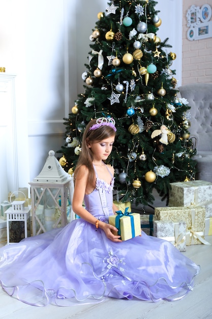 La chica del vestido morado con un regalo cerca del árbol de Navidad