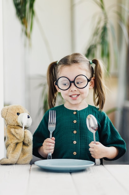 Chica en vestido de muselina verde esperando el desayuno con su amigo oso de juguete