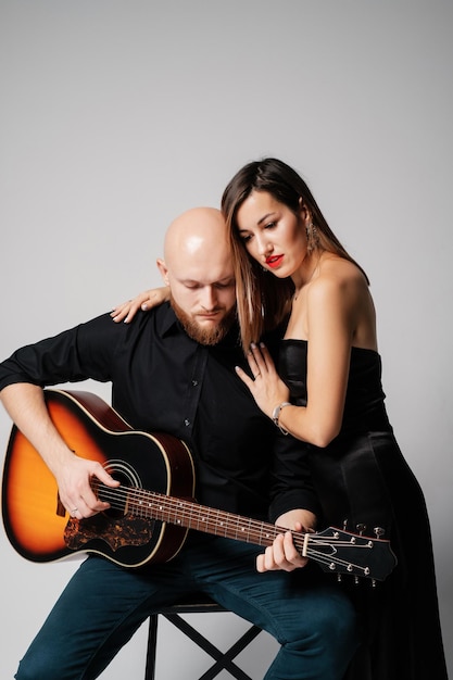 Una chica con un vestido negro abraza a un músico Hombre calvo barbudo con una guitarra