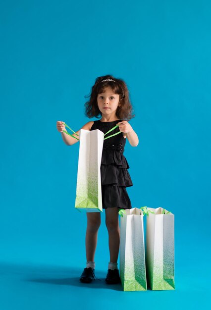 Chica en vestido negro con bolsas de papel ir de compras por descuentos sobre fondo azul.