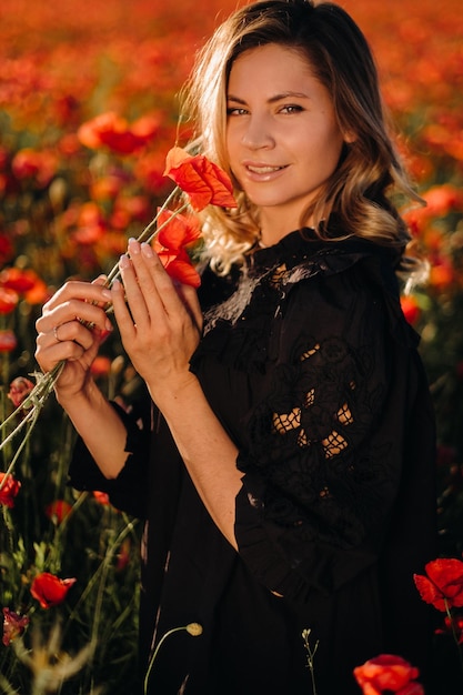 Una chica con un vestido negro en un campo de amapolas al atardecer