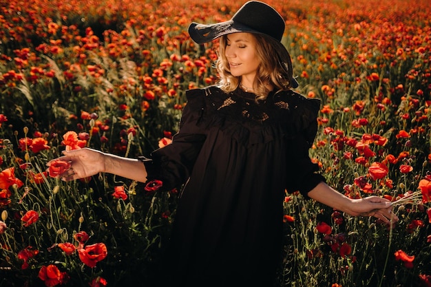 Una chica con un vestido negro y un sombrero en un campo de amapolas al atardecer