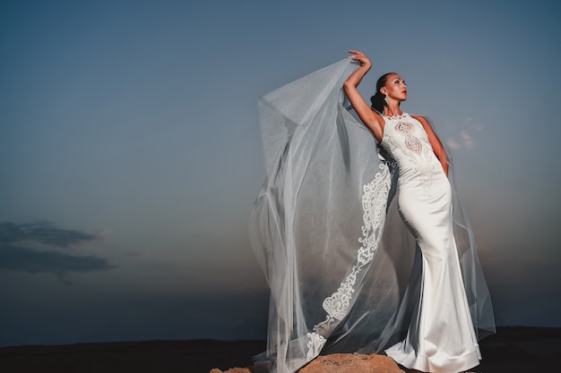 Chica en vestido de novia al aire libre en el cielo de la tarde. Novia y ceremonia. Modelo de elegancia y moda. Salón de belleza y moda nupcial. Mujer con vestido blanco al atardecer.