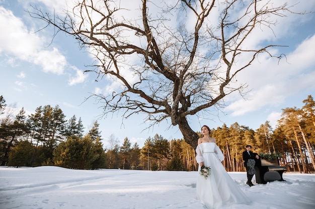 Una chica con un vestido de novia y un joven están de pie junto al piano. Fotografía de invierno