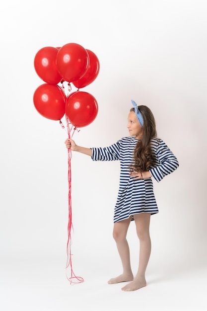 Chica con vestido a rayas sosteniendo un gran montón de globos rojos en la mano extendida y mirándolos