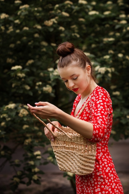 Chica en un vestido rojo con una bolsa de paja en la naturaleza en verano