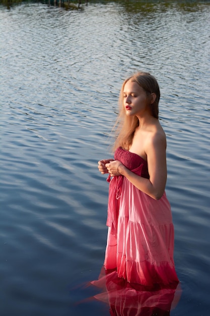 Una chica con un vestido rojo está de pie en el aguahermosa modelo de vacaciones en el lago