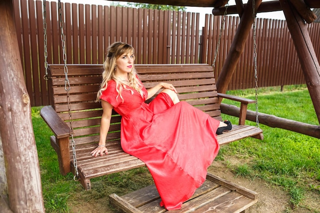 Chica en un vestido rojo posando en un columpio de madera