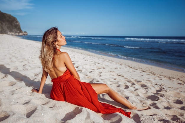 Chica en vestido rojo sentada sobre arena blanca