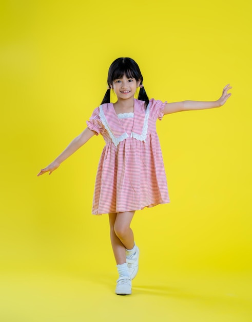 Una chica con un vestido rosa está parada frente a un fondo amarillo.