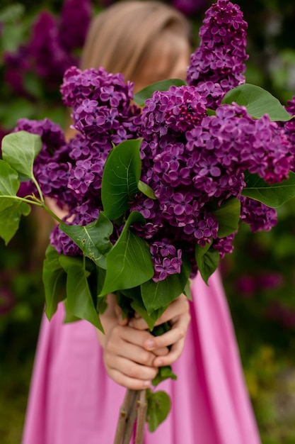 Una chica con un vestido rosa sostiene un ramo de lilas.