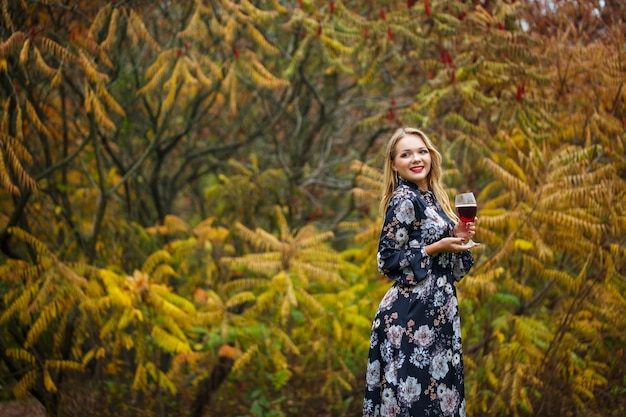 La chica del vestido sostiene una copa de vino tinto en el bosque de otoño