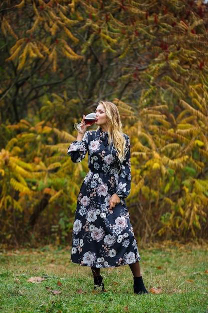 La chica del vestido sostiene una copa de vino tinto en el bosque de otoño