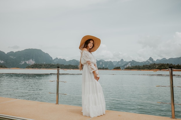 Chica de viaje feliz diversión en el muelle de madera con la selva y las montañas del bosque lluvioso del lago